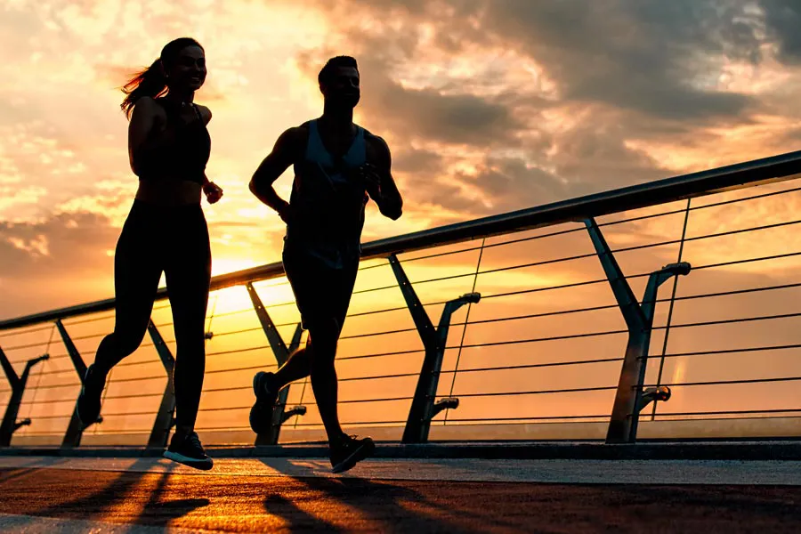 Amino-Blend-Vitamin-Injection-Clinic A couple running on a bridge, silhouetted by the sunrise. Get Amino Blend Vitamin Injection treatment from Christine Collins, MD in Westside/Beverly Hills.