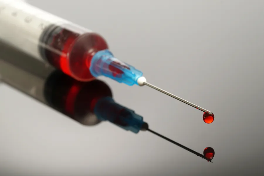 B12-Injection-Doctor A close-up of a medical syringe filled with a red liquid, capturing a drop of the liquid falling from the needle. Lipo-B12 Weight Loss Injecitons offered by Christine Collins, MD in Westside/Beverly Hills.
