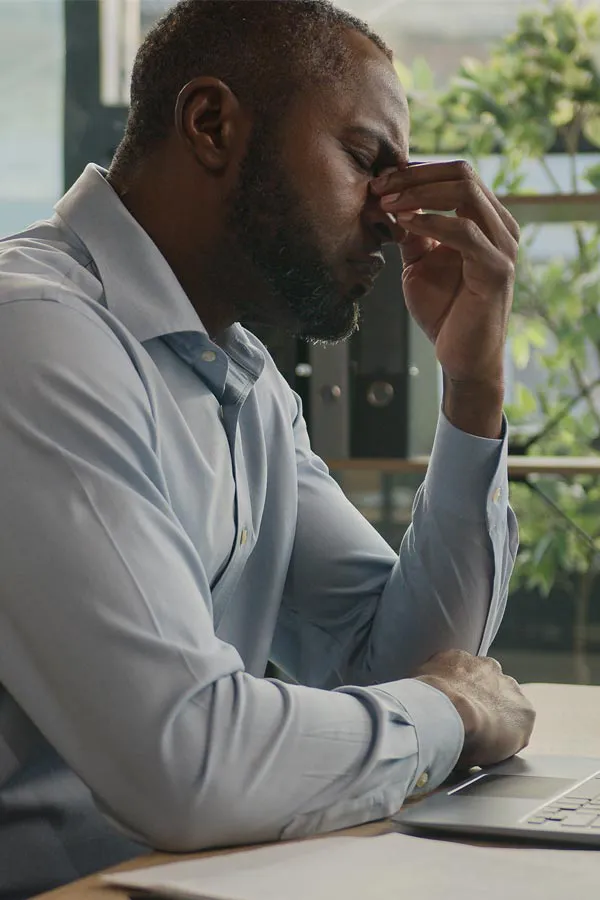 Chronic-Fatigue-Treatment A black man rubbing the top of his nose at his desk, in need of chronic fatigue treatment from Christine Collins, MD in Westside/Beverly Hills.