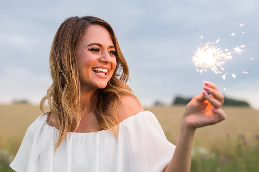 EMsella-for-Women-Clinic A cheerful young woman holding a lit sparkler in an open field at dusk satisfied with successful EMsella Pelvic Floor Strengthening treatment by Christine Collins, MD in Westside/Beverly Hills.
