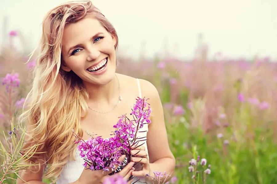 Gynecology-Clinic A smiling woman in a field holds a bunch of purple flowers. Get gynecology services from Christine Collins, MD in Westside/Beverly Hills.