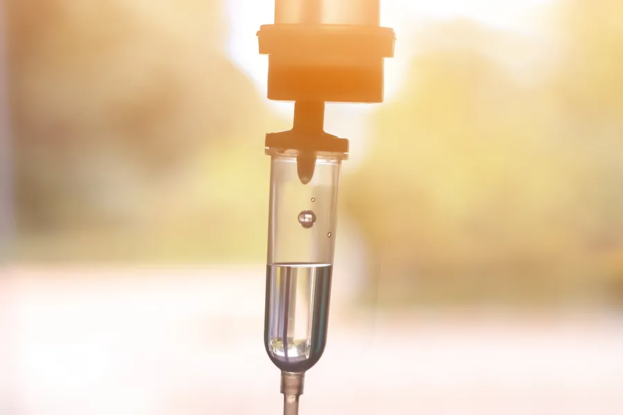 IV-Therapy-Doctor Close-up of an IV drip warmly lit by a window showing trees and a sunset, representing IV therapy from Christine Collins, MD in Westside/Beverly Hills.