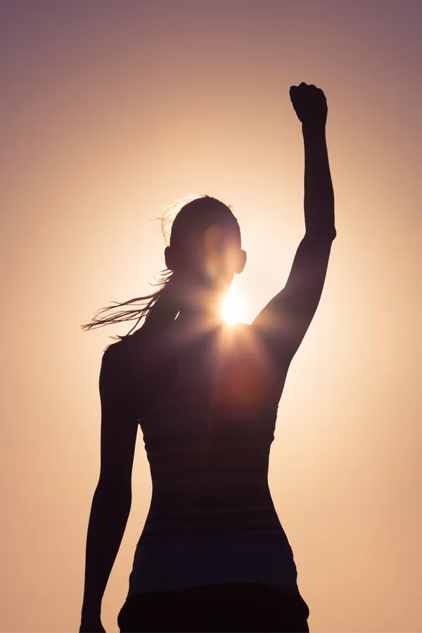 Methylene-Blue-IV-Therapy-Treatment A woman raises her fist in the air, silhouetted by the sun. Get methylene blue IV therapy from Christine Collins, MD in Westside/Beverly Hills.