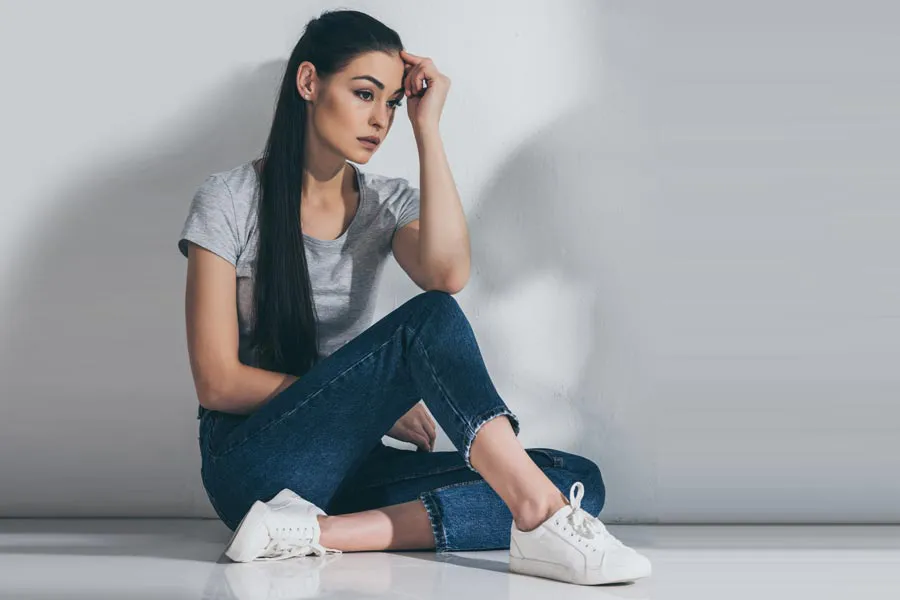 PCOS-Doctor A young brunette woman in a gray t-shirt and jeans sits against a gray wall with her head resting on her hand and a distressed expression. Get help for Polycystic Ovarian Syndrome (PCOS) from Christine Collins, MD in Westside/Beverly Hills.