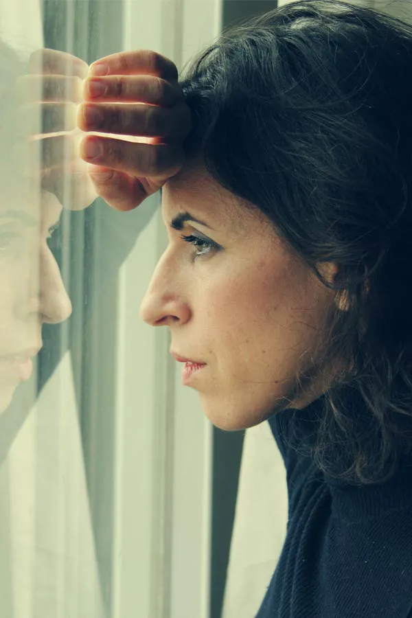 PCOS-Treatment A brunette woman in a thin dark turtleneck looks out the window with a serious expression, suffering from PCOS. Get treatment for Polycistic Ovarian Syndrome/PCOS from Christine Collins, MD in Westside/Beverly Hills.