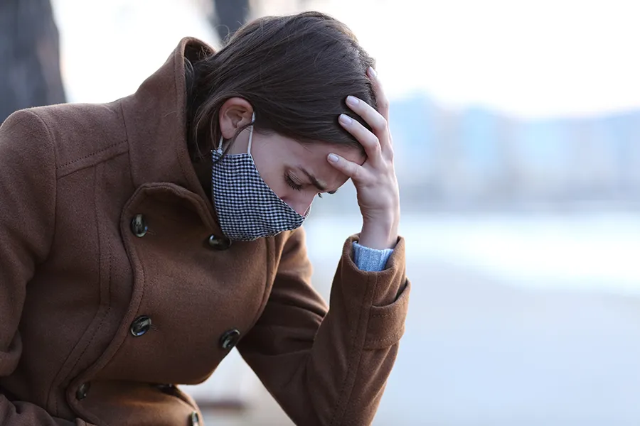 Post-Covid-Clinic A woman in a mask sits outside with her hand on her forehead in pain. Get long covid treatment from Christine Collins, MD in Westside/Beverly Hills.