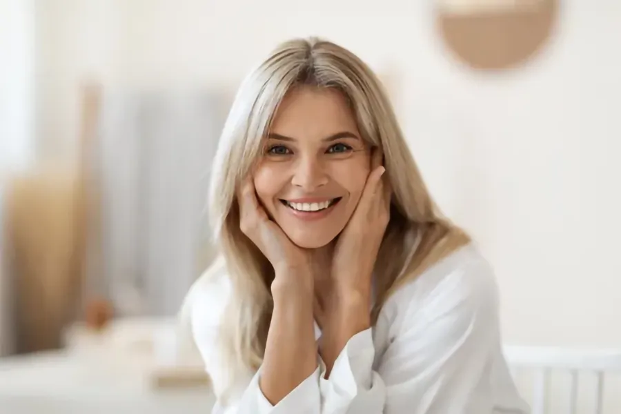 Vaginal-Atrophy-Clinic A middle-aged woman sits smiling in her living room. Schedule treatment for vaginal atrophy from Christine Collins, MD in Westside/Beverly Hills.