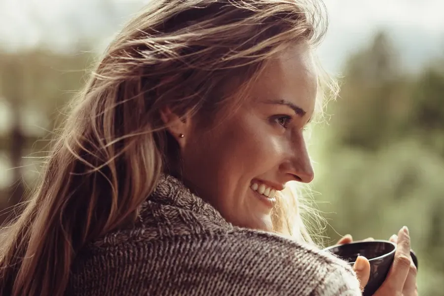 Womens-Health-Exams-Clinic A middle-aged blonde woman in a sweater drinks tea, framed by a forest horizon. Get comprehensive women's health exams from Christine Collins, MD in Westside/Beverly Hills.